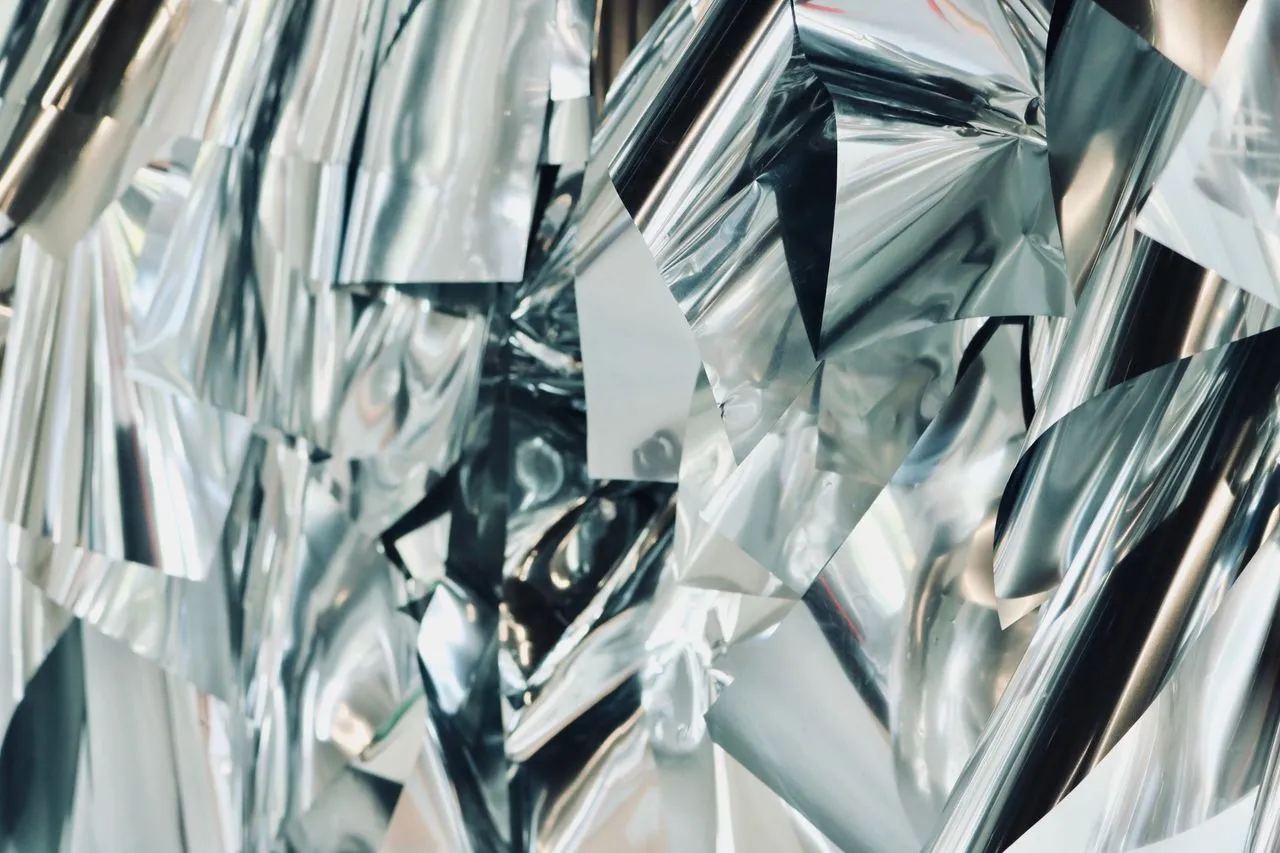 Sheets of crumpled aluminum foil catching the light in overlapping silver folds