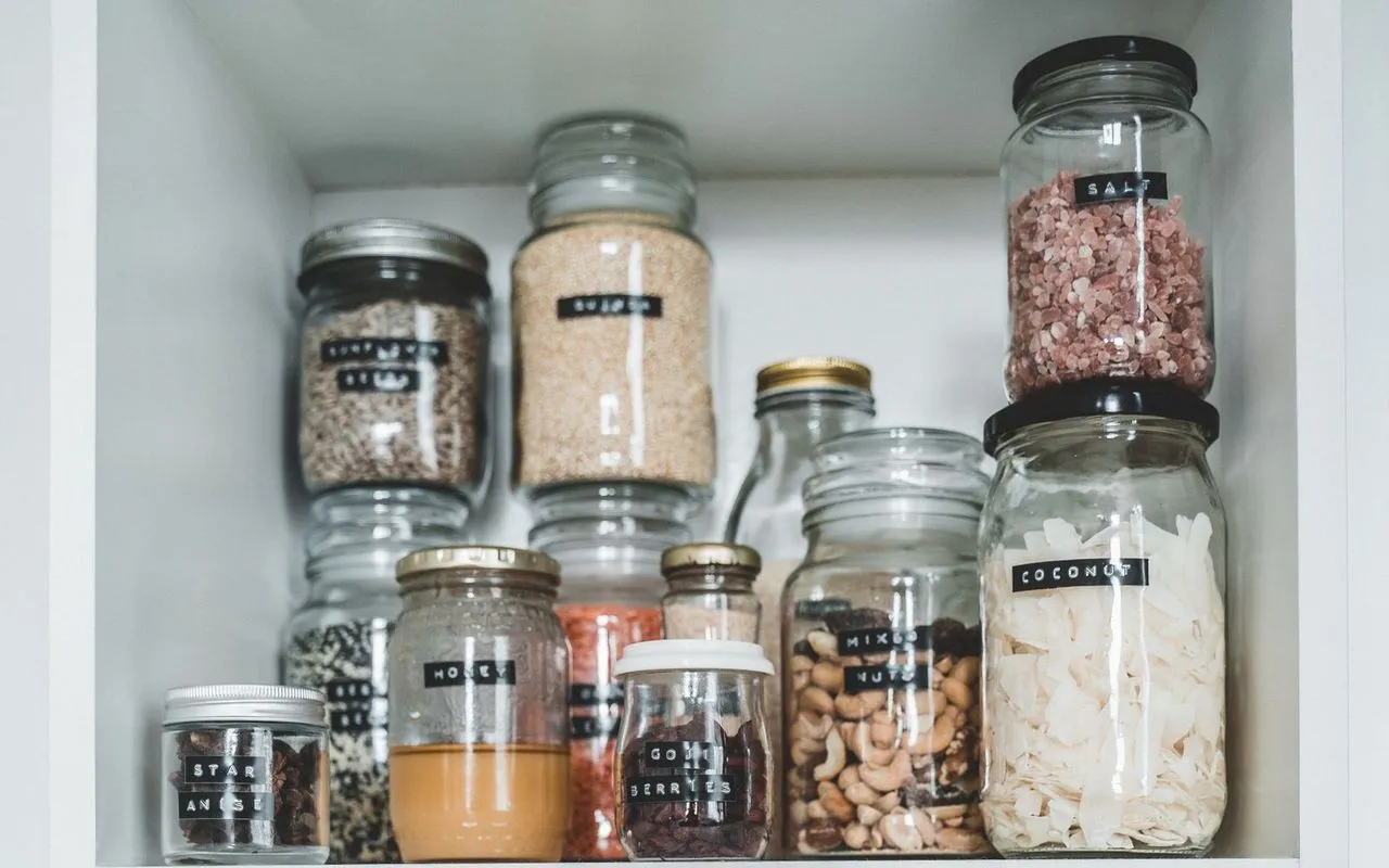 Labeled glass jars of dry goods organized on white pantry shelves