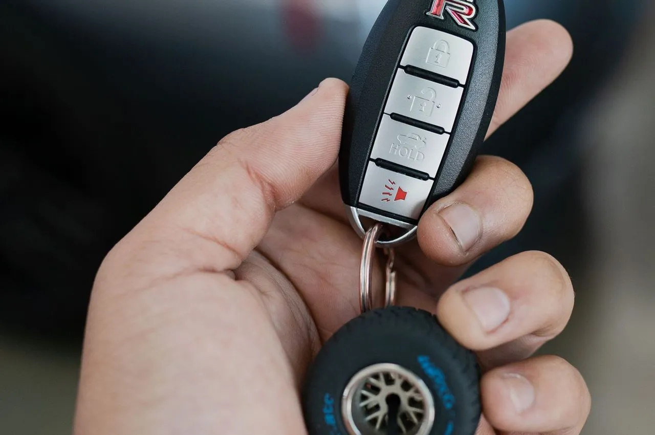 Hand holding a modern keyless entry fob with a car blurred in the background