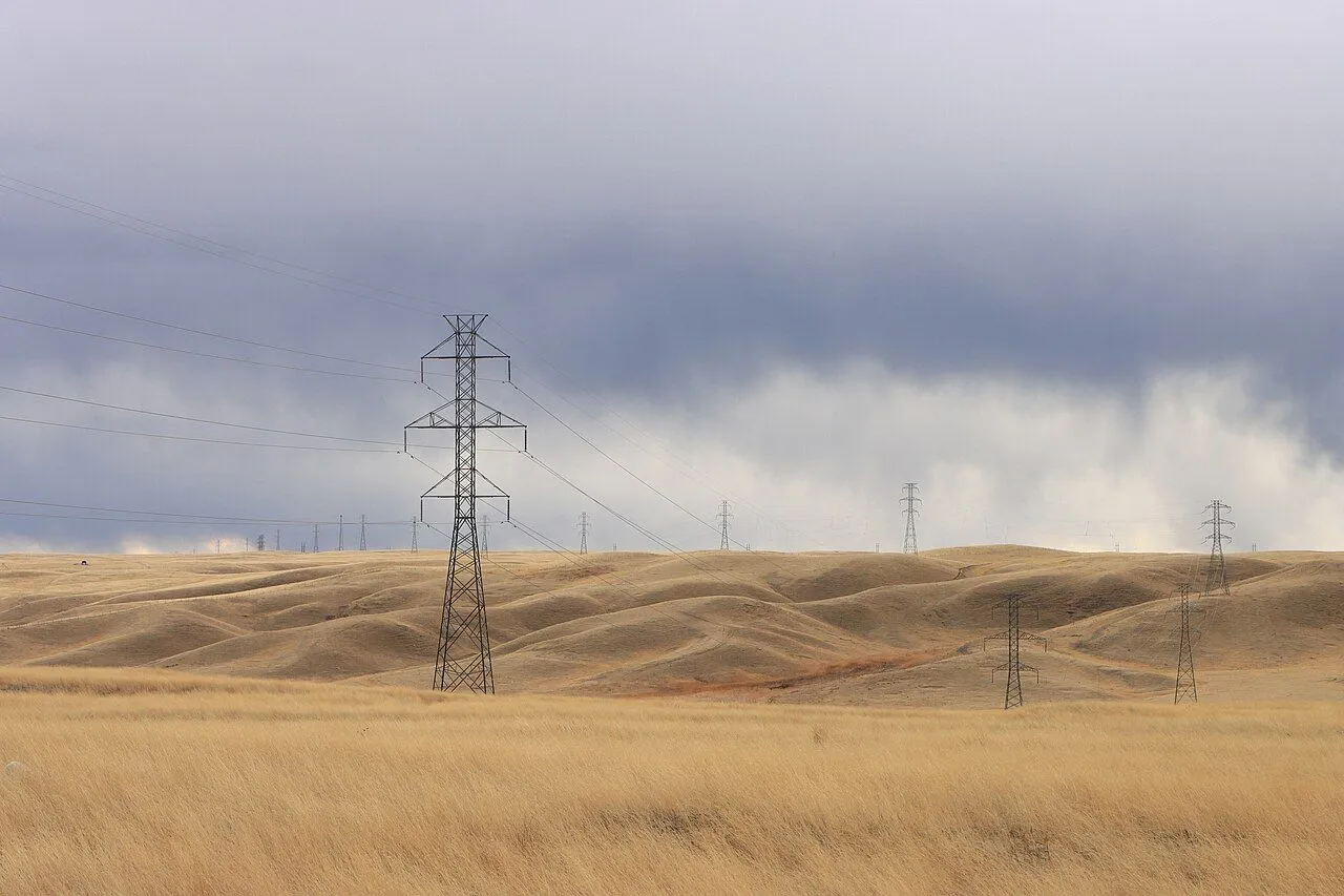 High-voltage transmission towers crossing open grassland under dark storm clouds