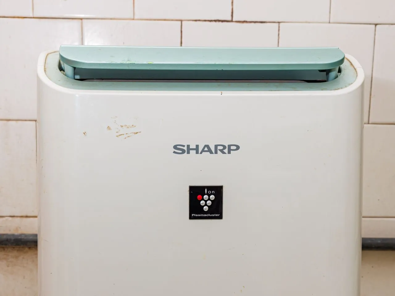 White portable dehumidifier with control panel, standing on a tiled floor