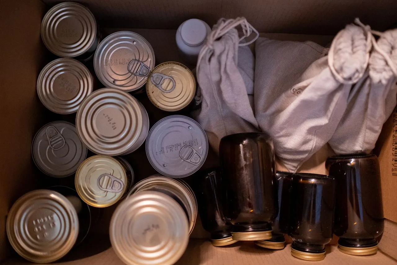 Top-down view of a box packed with canned goods, jars, and cloth food sacks