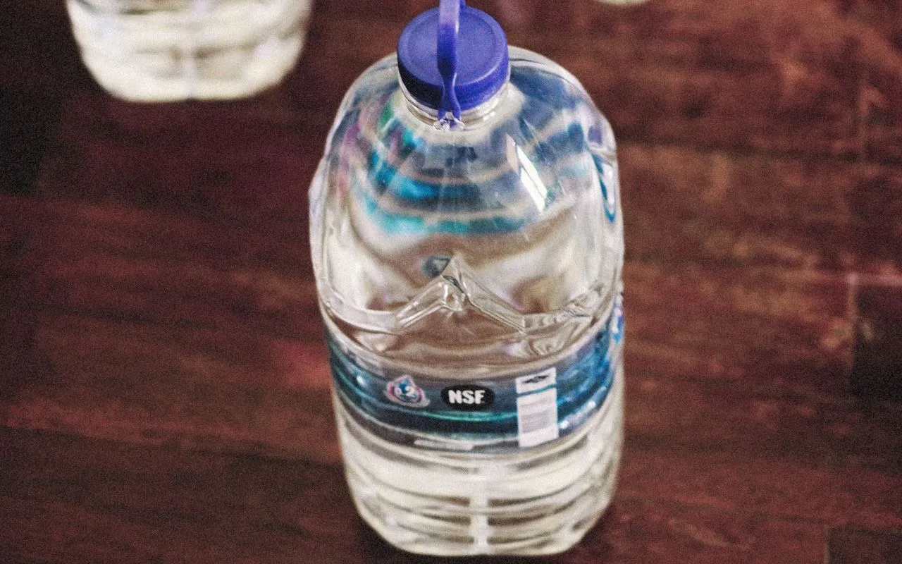 Bottled water jugs stored on a dark wooden floor, the front jug labeled with an NSF mark